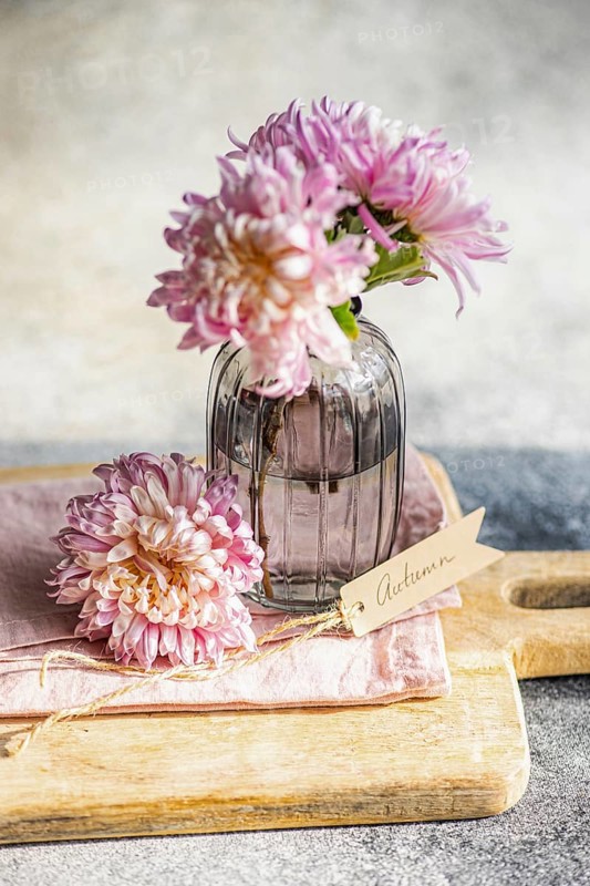 Elegant chrysanthemums in a textured glass vase, set on a wooden board, create an autumnal theme A handwritten Autumn tag adds a charming touch to this serene display
