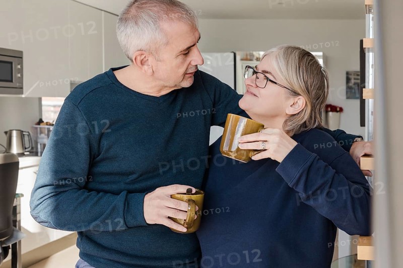 A senior couple, relaxed and happy, enjoying coffee together They share affectionate glances in a cozy kitchen setting, reflecting love and companionship in later years