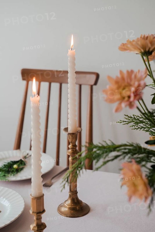 A serene dinner table setup featuring two lit taper candles in brass holders, complemented by fresh flower decor and subtle tableware, ideal for a sophisticated dining atmosphere