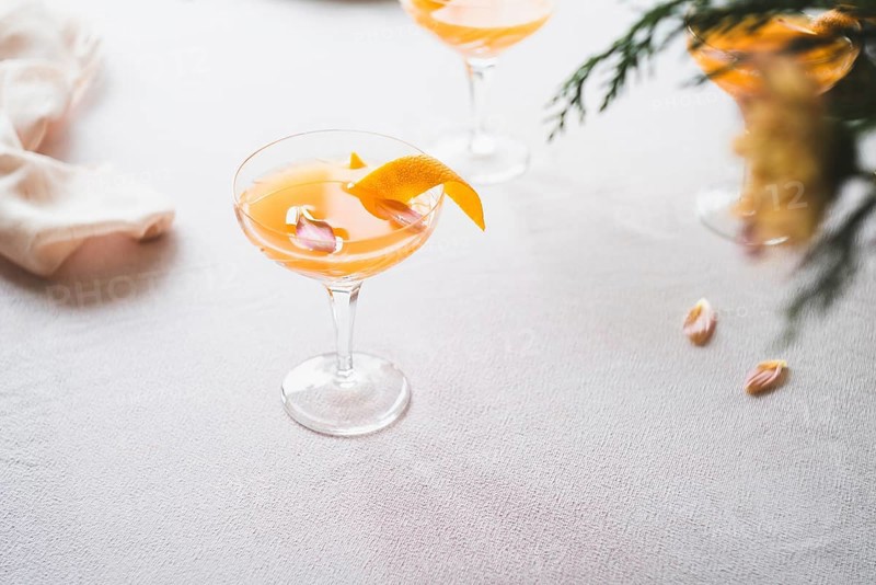 Elegant mandarin cocktail served in a stemmed glass, garnished with a twist of orange zest, on a textured white tablecloth. Subtle lighting enhances the soothing ambiance, perfect for a refreshing moment