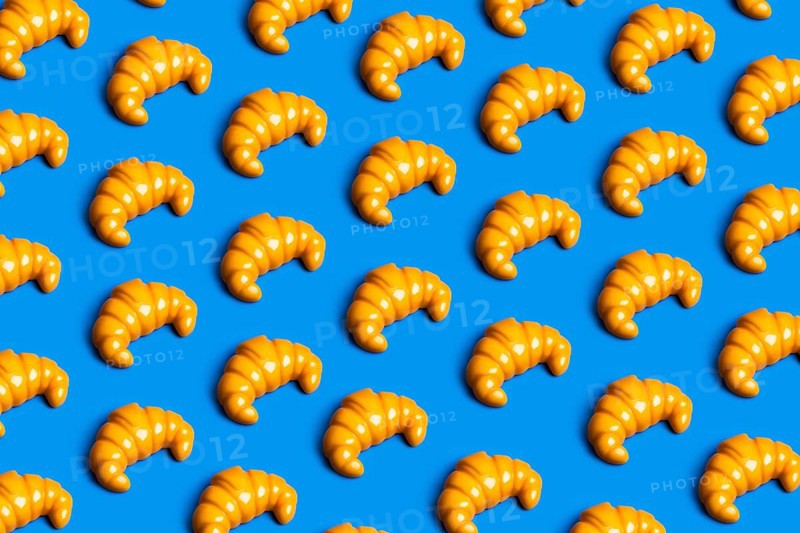 A vibrant pattern of plastic croissants against a blue background, symbolizing the clash between junk food consumption and diet culture in modern society