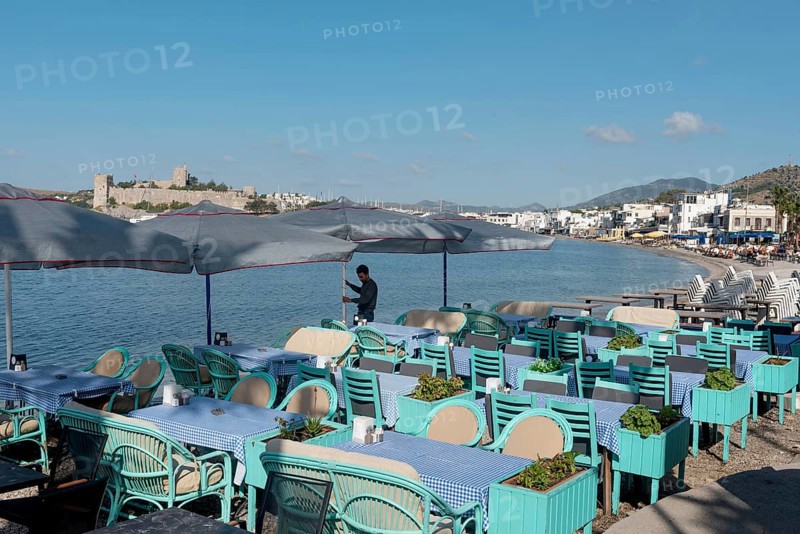 Bodrum, Mugla, Turkey. April 21st 2022 A waiter prepares tables on the beach side cafe in Bodrum harbour with Bodrum Castle in the background, the Aegean coast of south west Turkey