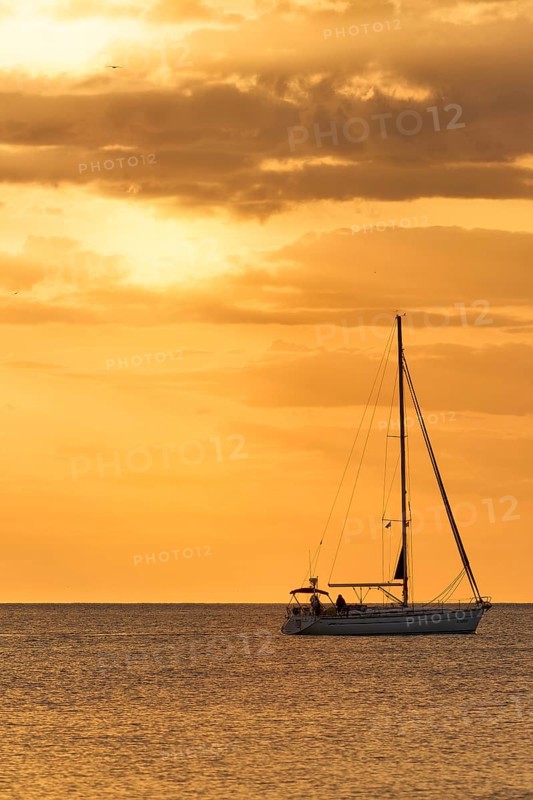 A serene view of a sailboat gliding across calm waters at sunset, surrounded by golden skies, captured near La Zenia, Cabo Roig, Orihuela Costa, Alicante, Spain