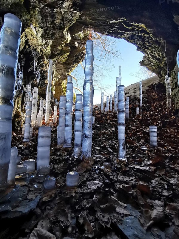 Icicles rise in a brightly lit rock cave with colorful leaves, hiking in the Franconian Forest nature park Park