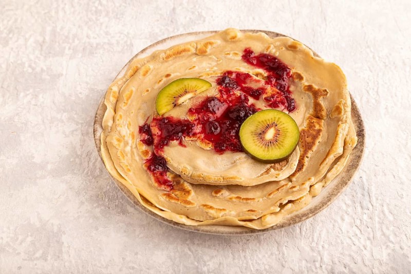 Stack of Plain Fried pancakes with jam and kiwi on gray concrete. side view, close up