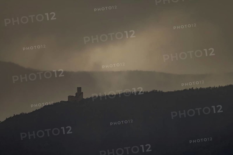 The structure is on a mountain. The sky is cloudy and sunlight is shining in the distance. The scenery shows a dark and mysterious atmosphere. Bas Rhin, Alsace, France