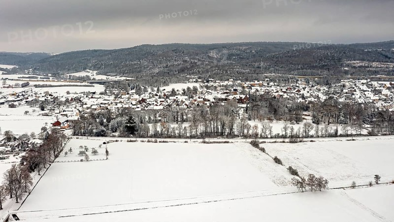 Aerial view of a snowy landscape with fields, hills and a village under grey sky, Herleshausen in northern Hesse