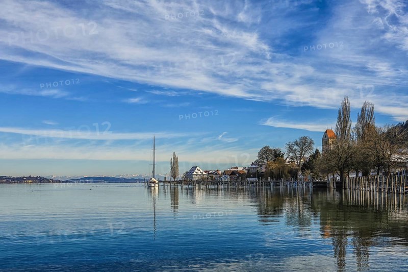 Calm lake in winter with a sailboat on the shore, surrounded by houses and trees, under a cloudy blue sky, Lake Constance, Überlinger See, Bodman-Ludwigshafen, Konstanz district, Baden-Württemberg, Germany