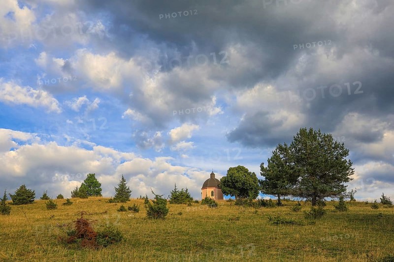 A small chapel stands on a green hill under a cloudy sky with trees, Upper Danube nature park Park, Josefskapelle, Alter Berg Landscape Protection Area, Böttingen, Großer Heuberg, Tuttlingen District, Baden-Württemberg, Germany