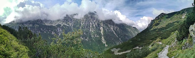 A trail leads through impressive mountain scenery, panoramic peaks covered with green slopes and clouds, hiking in the High Tatras National Park, Carpathian Mountains, Poland