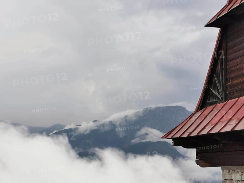 View of a mountain peak through clouds, with part of a wooden building in the foreground, Zakopane, hiking in the High Tatras National Park, Carpathian Mountains, Poland