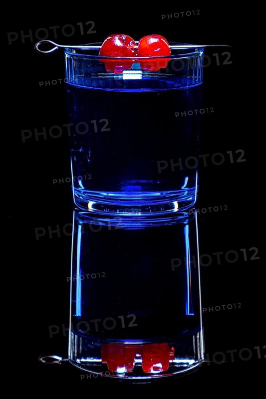 Blue drink in a glass with cherries, against black background and reflection