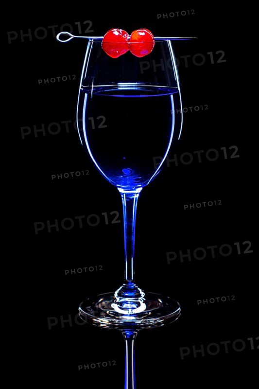 Blue drink in a wine glass with cherries, black background and reflection