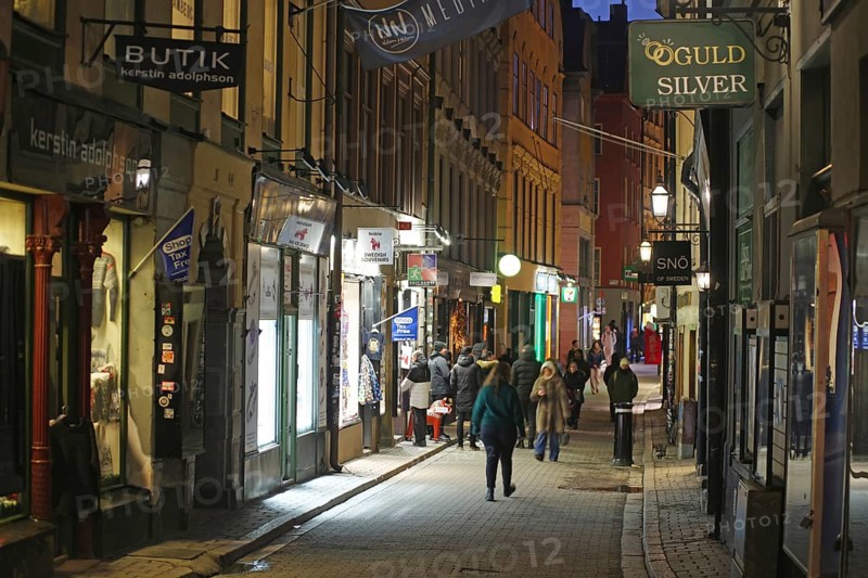 Busy street with pedestrians and illuminated shops at dusk, Gamla Stan, Old Town, Stockholm, Sweden