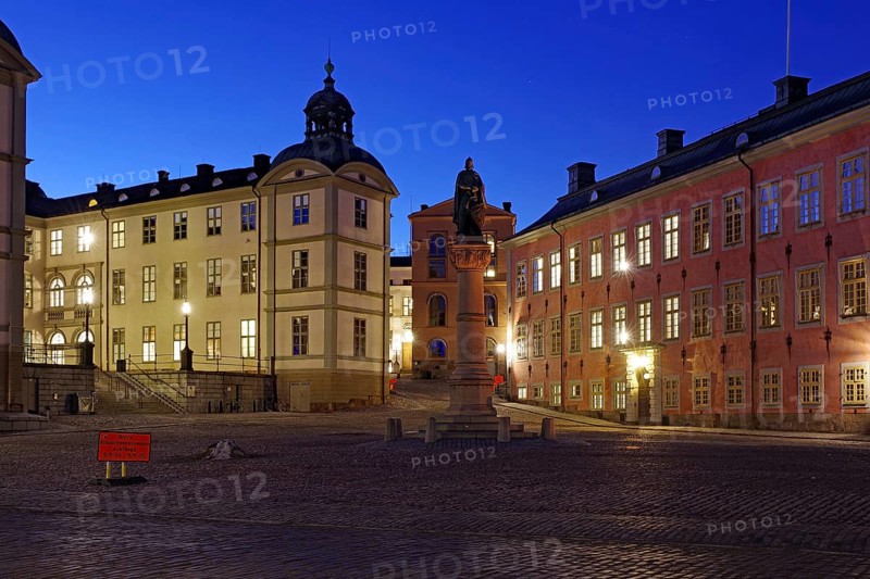 An illuminated town square with historic buildings and a memorial at dusk, Riddarholmen, Stockholm, Sweden