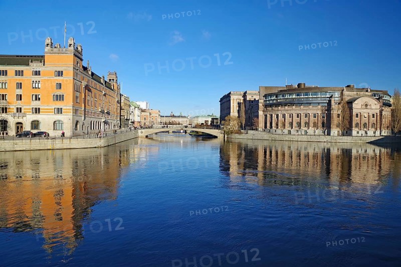Clear river water with reflecting buildings and a bridge under a blue sky, Government District, Stockholm, Sweden