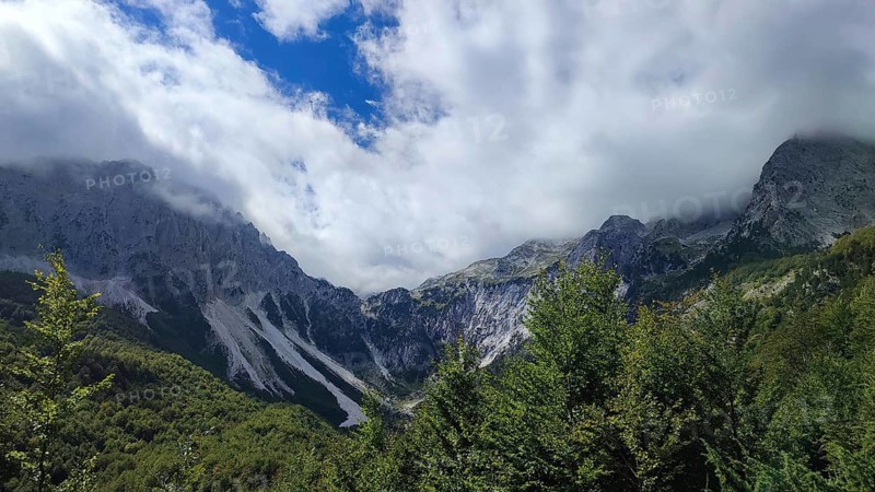 Mountain panorama, majestic mountain landscape with clouds and thick forests under blue sky, Peaks of the Balkans, hiking in the Albanian Alps National Park, Albania