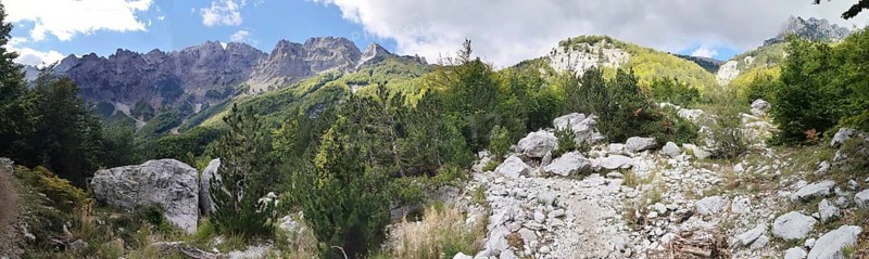 Panorama, rocky path surrounded by trees and mountains under a partly cloudy sky, Peaks of the Balkans, hiking in the Albanian Alps National Park, Albania