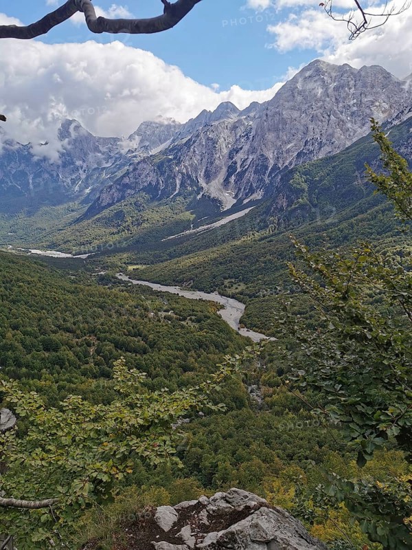 Wide view of a green valley with a river and high mountains under cloudy sky, Peaks of the Balkans, hiking in the Albanian Alps National Park, Albania