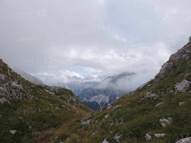 Snowy valley surrounded by mountains, partly obscured by clouds and fog, Peaks of the Balkans, hiking in the Albanian Alps National Park, Albania