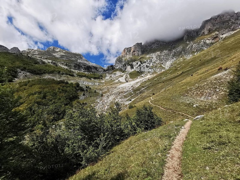 Trail through a mountainous landscape with dramatic clouds in the sky, Peaks of the Balkans, hiking in the Albanian Alps National Park, Albania