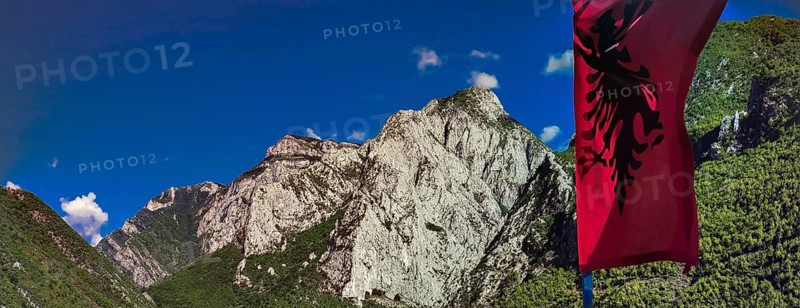 Alpine landscape with an Albanian flag and majestic mountains under blue sky, Peaks of the Balkans, hiking in the Albanian Alps National Park, Albania