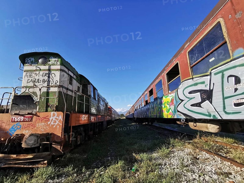 Graffiti-painted locomotive next to abandoned train row, sunny day, Albania