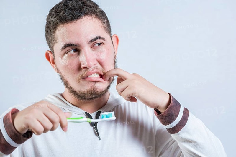 Young man with tooth sensitivity holding a toothbrush isolated. Man suffering from gum pain holding brush