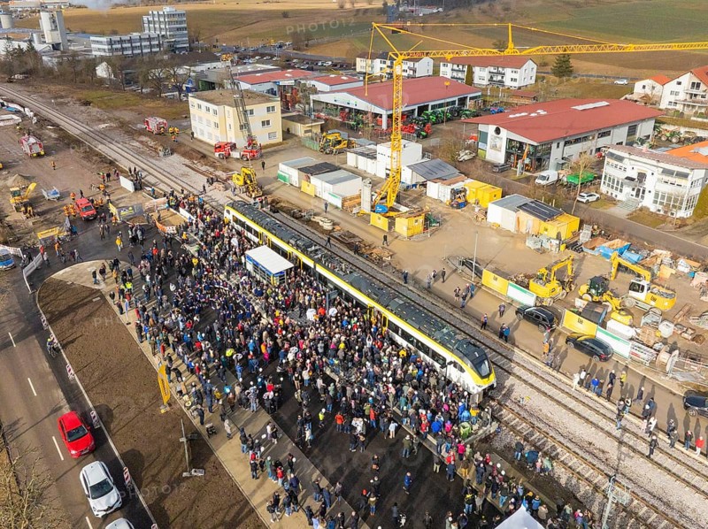 People gather around a train on a construction site, aerial view with landscape in the background, opening of the Hermann Hesse Railway, Calw, Germany