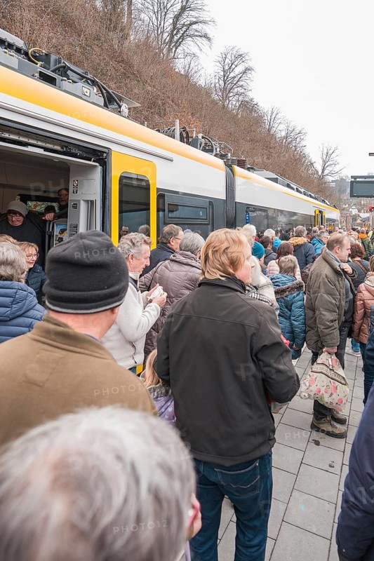People board a yellow train standing at a platform in an urban area, opening of the Hermann Hesse Railway, Calw, Germany