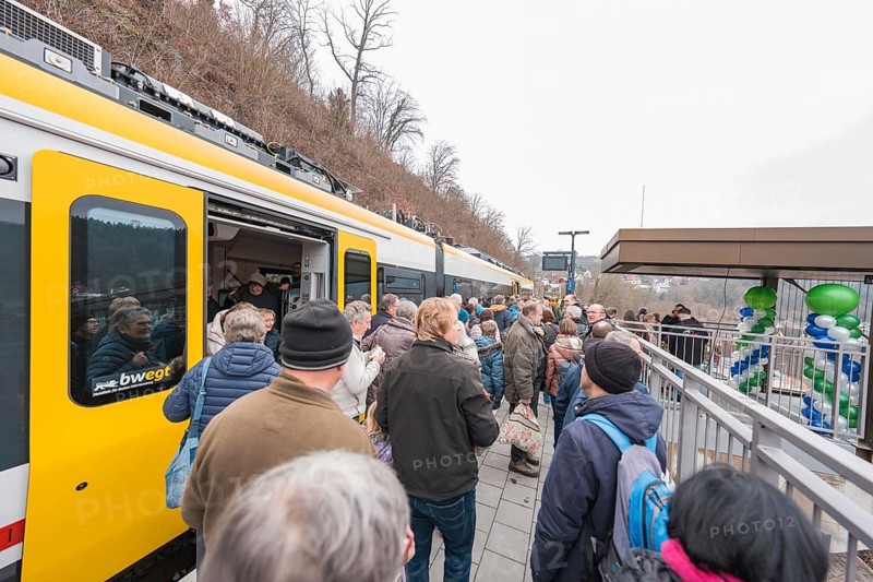 People standing on a platform next to a decorated train, platformside celebration, opening of the Hermann Hesse Railway, Calw, Germany