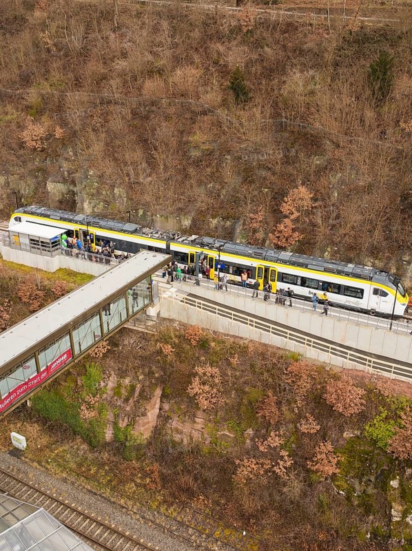Train at a train station along a hill with bare trees and people waiting, opening of the Hermann Hesse Railway, Calw, Germany
