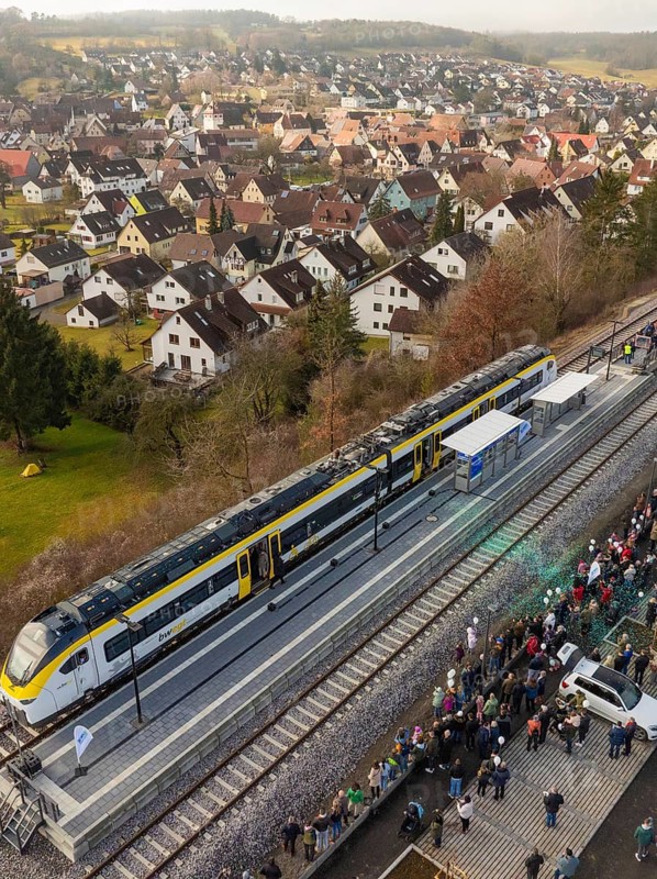 A train stops at the village station and many people are gathered. In the background, the village stretches over rolling hills, opening of the Hermann Hesse Railway, Calw, Germany