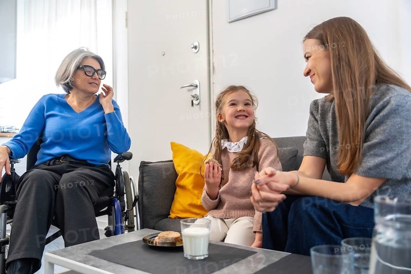 Loving three generation familygrandmother in wheelchair, mother and young daughter sharing smiles, conversation and gentle care during a warm, relaxed visit at home