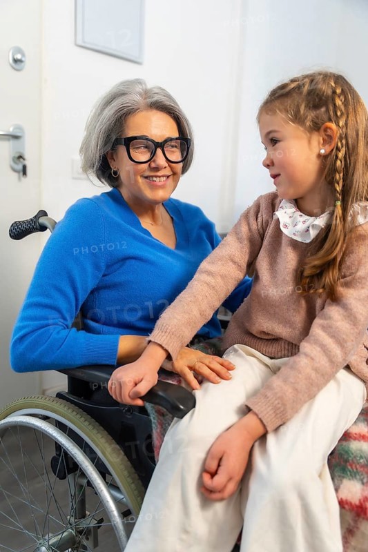 Granddaughter tenderly interacting with her smiling grandmother in a wheelchair, symbolizing strong family bonds, intergenerational love, and compassionate care during a visit