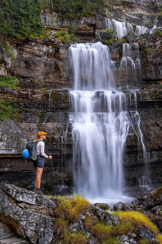 Young pretty hiker standing on rocks in front of Cascata di Mezzo waterfall, long exposure, Vallesinella, Brenta, Trentino, Italy
