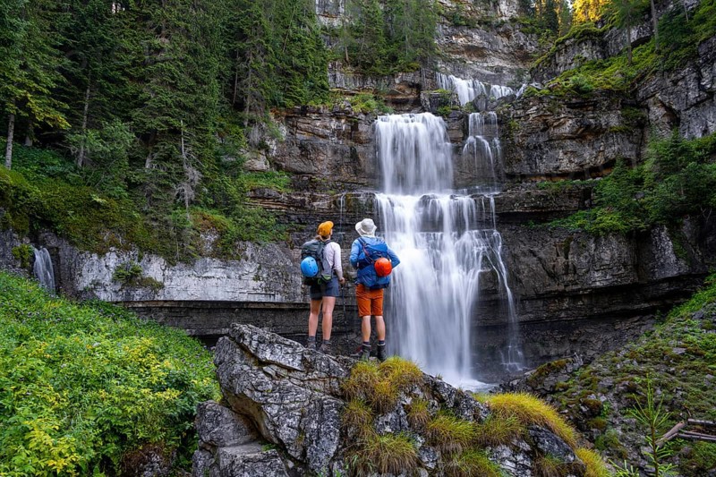 Young pretty hiker standing on rocks in front of Cascata di Mezzo waterfall, long exposure, Vallesinella, Brenta, Trentino, Italy