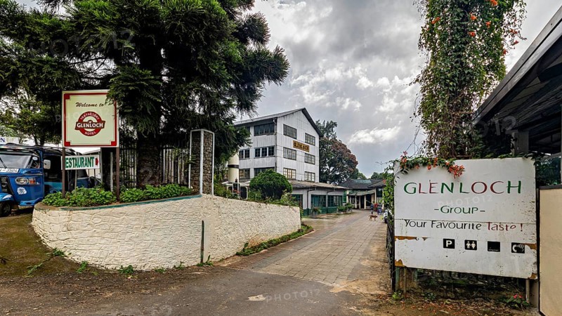 Entrance area of a facility with signs, trees and cloudy sky, tea factory in the mountains near Kandy Sri Lanka