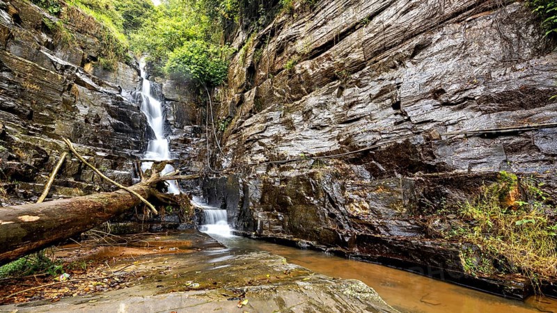 A narrow waterfall flows in a rough environment from rocks surrounded by forest, waterfall in the mountains of Kandy in Sri Lanka
