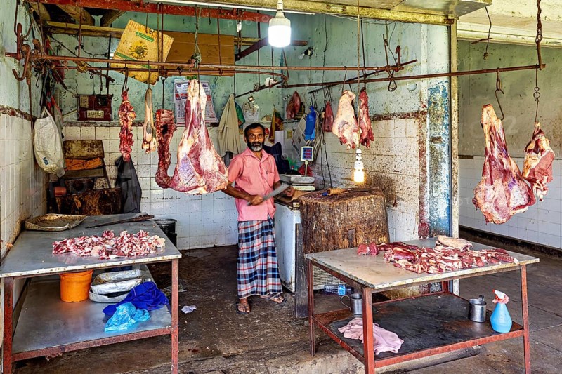 Butcher in traditional slaughterhouse with pieces of meat hanging on hooks, The old market halls of Kandy in Sri Lanka