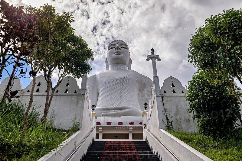 Impressive Buddha statue on the temple grounds, surrounded by stairs and trees, with cloudy sky, white Buddha statue in a temple in Kandy in Sri Lanka