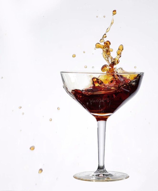 A brown liquid sloshes back and forth in a cocktail glass, studio shot against a white background