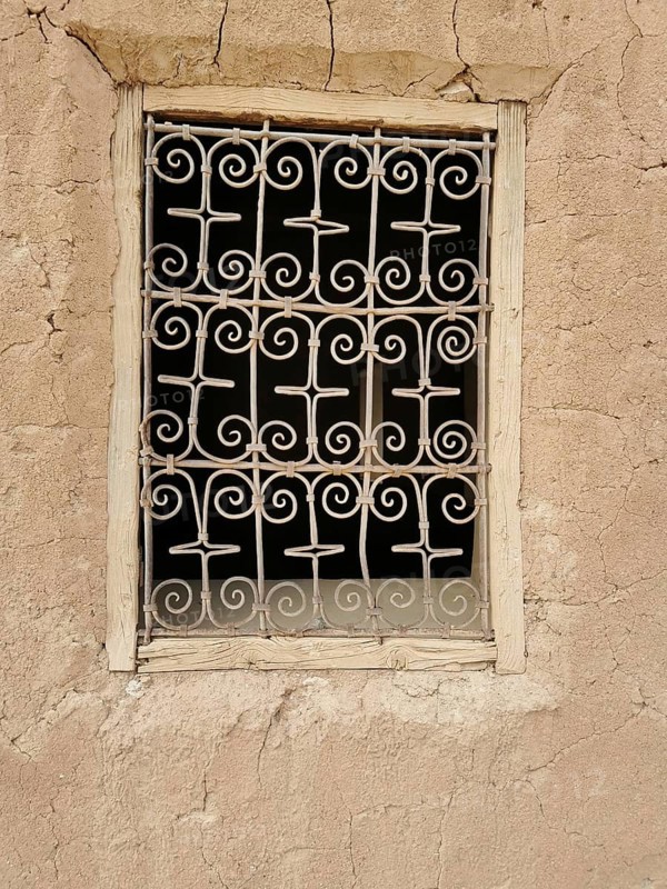 Decorated window screen in a crumbling, beige clay wall with rustic ambiance, Morocco