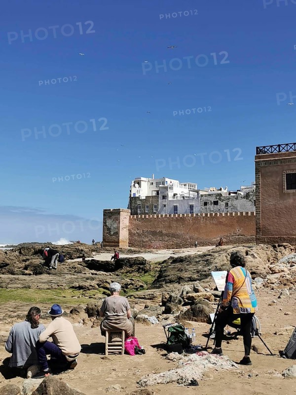 Painters paint the city view on the coast in front of old city walls and rocks under a blue sky, Essaouira, Marakesh