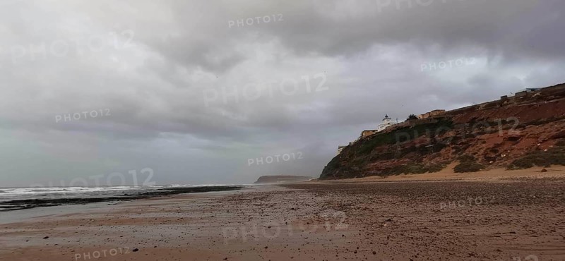 Empty beach with cloudy sky and rocky coast in the background, Morocco