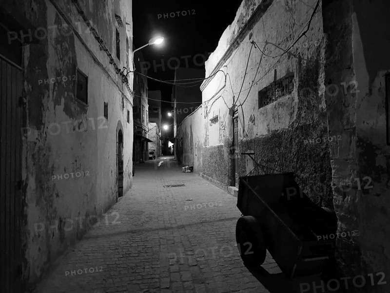 Abandoned old alley in nighttime darkness, faintly lit by black and white lanterns, Essaouira, Morocco