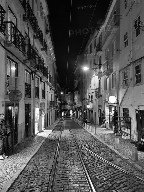 Nighttime scene of a narrow paved street surrounded by tall buildings in black and white, Lisbon, Portugal