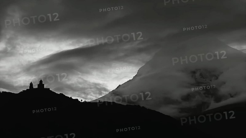 Dramatic silhouette of church buildings in front of a cloud-covered mountain, Kazbegi, Stepantsminda, Georgia