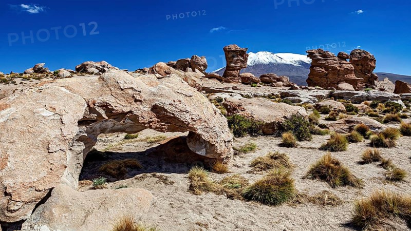 Desert landscape with stone arch and snow-covered mountain in the background under bright blue sky, The landscape of the Altiplano in Bolivia