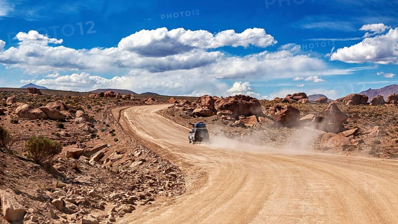 A vehicle drives on a dusty desert road through rocky landscapes under blue skies, The landscape of the Altiplano in Bolivia